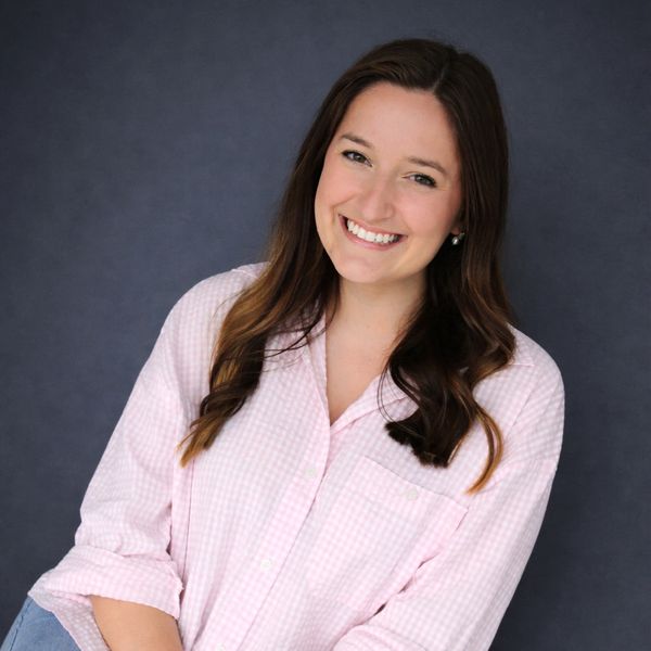 A smiling woman in a light pink checkered shirt against a dark backdrop.