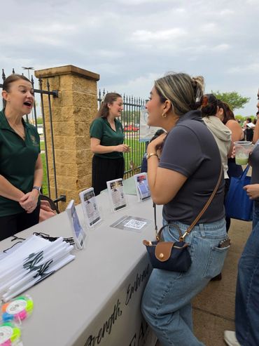 A woman talks to two people at an outdoor info table during an event.