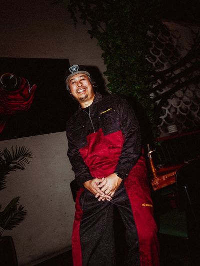 Smiling man in a black and red outfit and cap posing indoors.