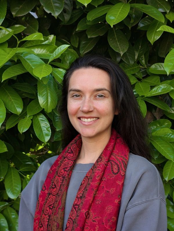 Smiling woman in front of leafy background wearing a red scarf.