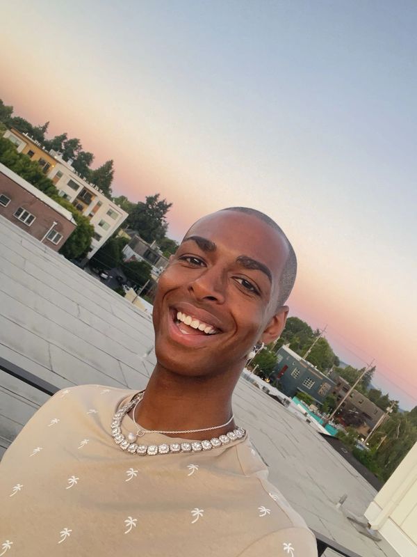 Smiling man wearing a beige shirt and silver jewelry during sunset.