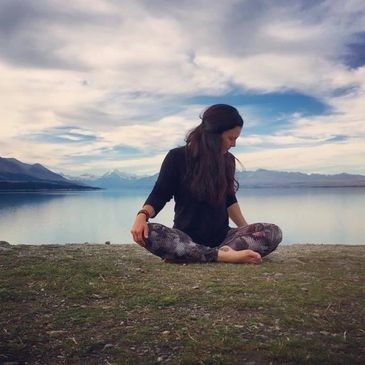 Woman practicing yoga by a serene lake with mountains in the background.
