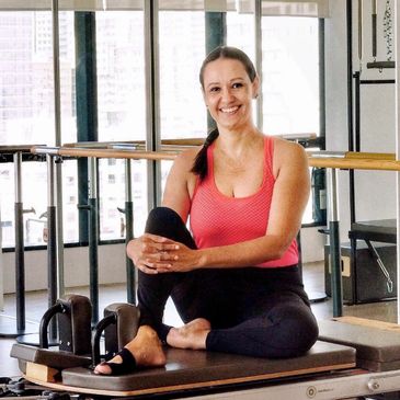 A woman in workout clothes sitting and smiling on a Pilates reformer machine.