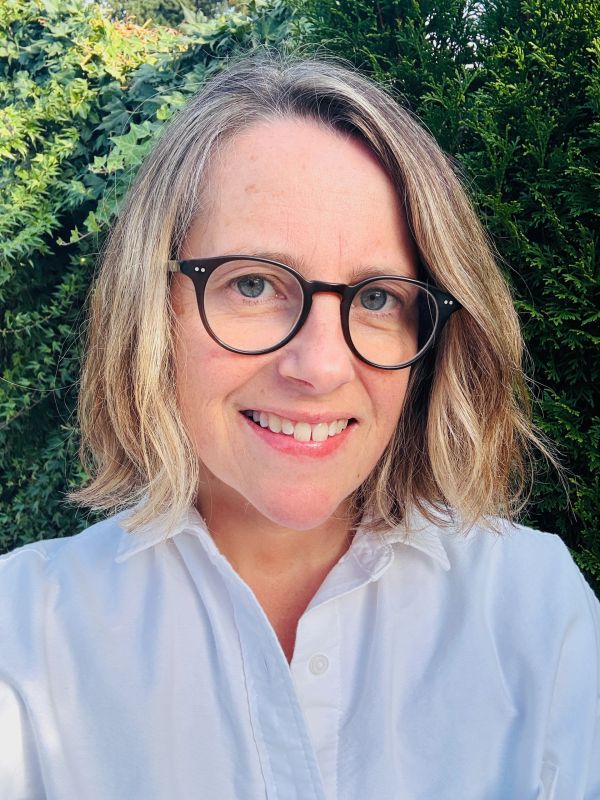 Smiling woman with glasses and blonde hair outdoors.