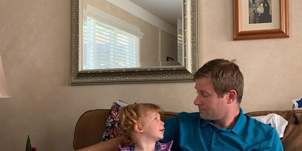 A man and a young girl share a moment on a brown couch in a cozy living room.