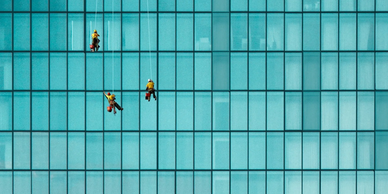 Three window cleaners suspended on the side of a skyscraper. Photo by Victor on Unsplash
