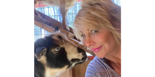 A woman smiling closely with a black and white goat inside a wooden pen.