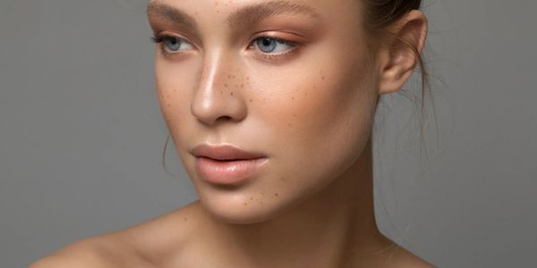 Close-up of a young woman with natural makeup and freckles on a gray background.