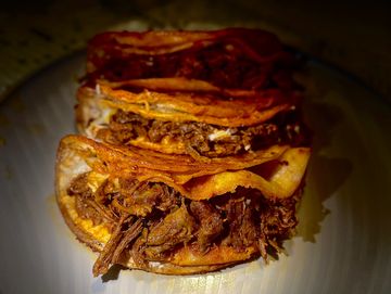 Three crispy tacos filled with seasoned shredded meat and topped with sauce.