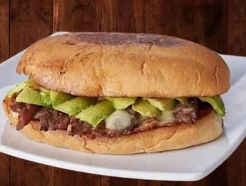 A sandwich with grilled meat, avocado slices, and cheese on a toasted bun.