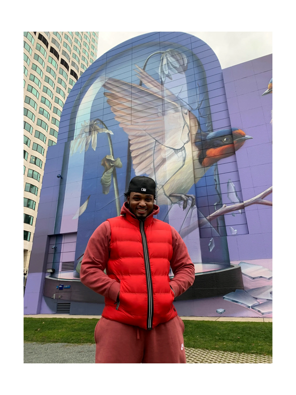 Darien Davis in Boston, Massachusetts Infront of a mural of a bird and flower.