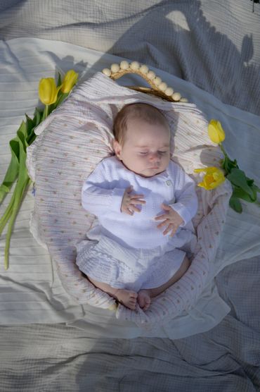 Sleeping baby surrounded by yellow tulips on a soft blanket.