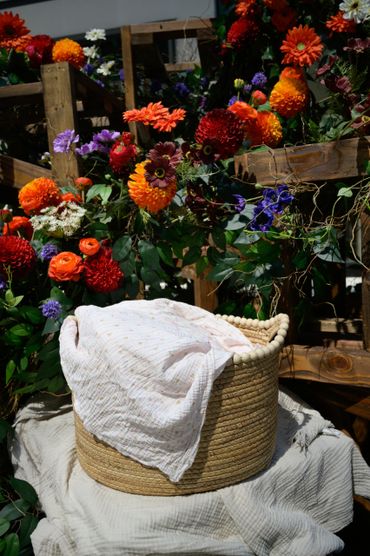 A wicker basket with a white cloth surrounded by vibrant flowers.