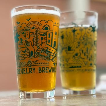 Two craft beers in brewery logo pint glasses.