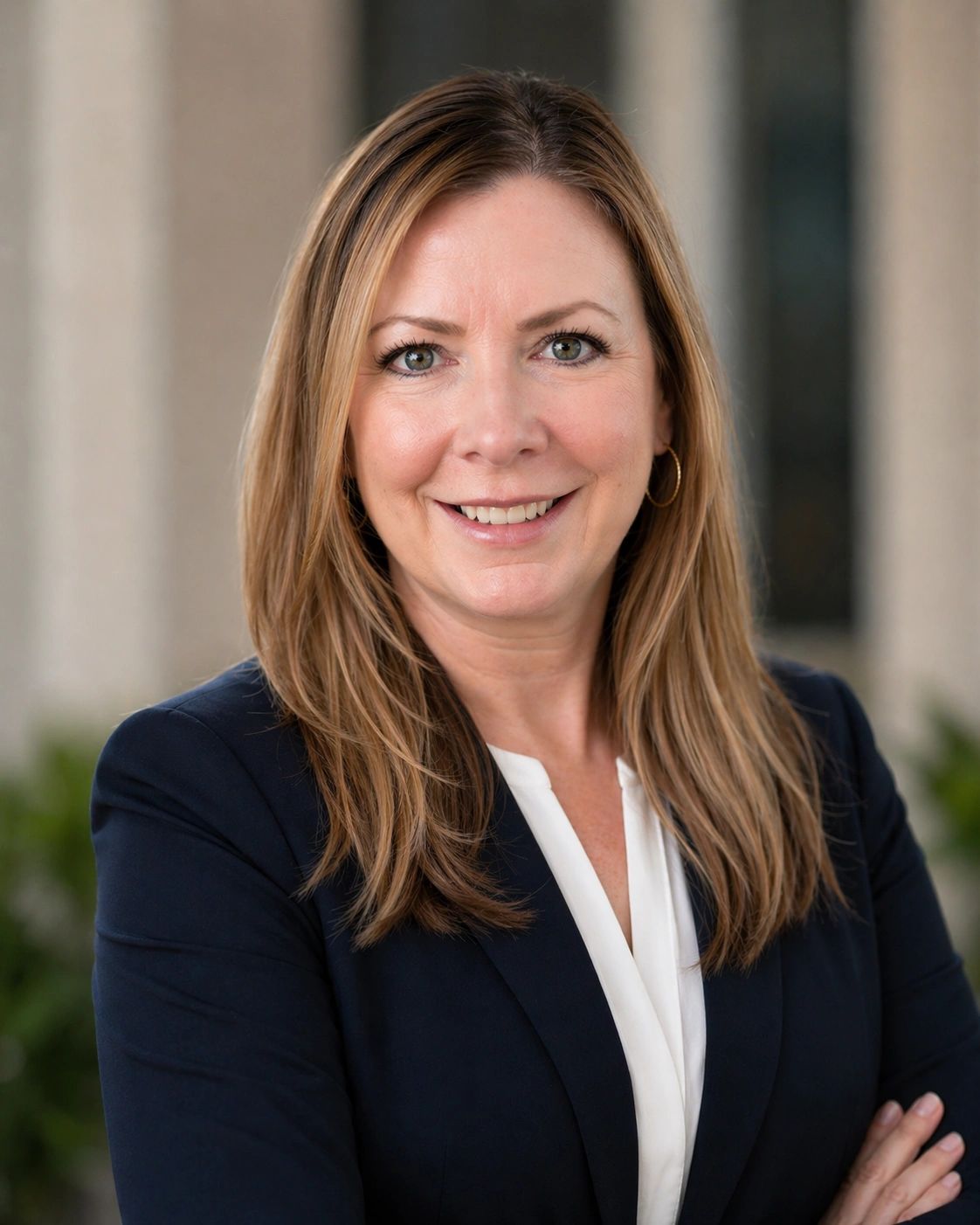 Confident woman in professional attire smiling with arms crossed.