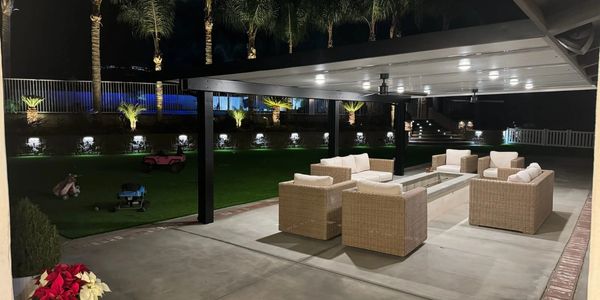 Outdoor patio with wicker furniture and fire pit under a covered roof at night.