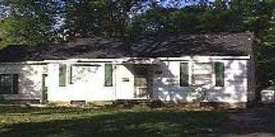 Small white house with green shutters in a shaded yard.