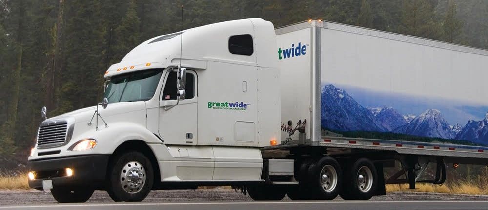 White semi-truck with a mountainous landscape image on its trailer, parked by a forested roadside.