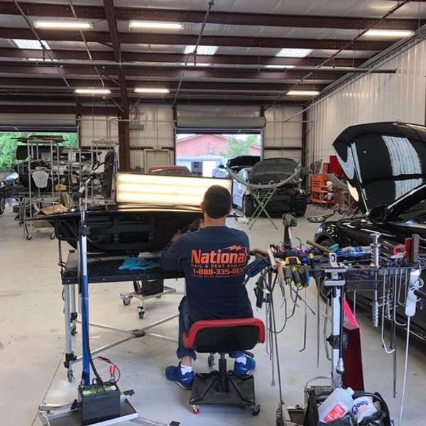 Technician working on car dent repair in a spacious garage.