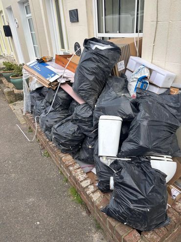 Pile of black garbage bags and discarded items outside a house.