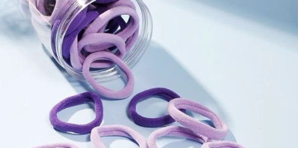 Purple and lilac hair ties spilling from a jar onto a surface.