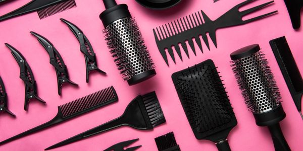 Black hair styling tools arranged on a pink background.
