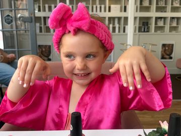 Little girl in pink robe and headband showing her nails.