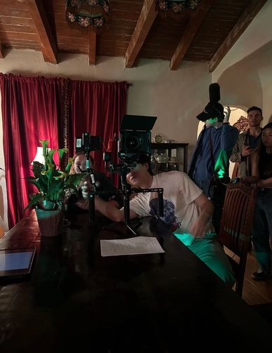 Film crew setting up a camera on a table in a dimly lit room with red curtains.