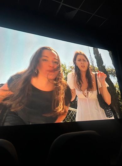 Two women shown on a movie screen in a theater, one looking surprised.
