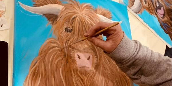 An artist painting a detailed Highland cow portrait on canvas.