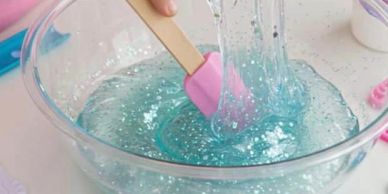 Mixing clear blue slime in a glass bowl with a pink spatula.