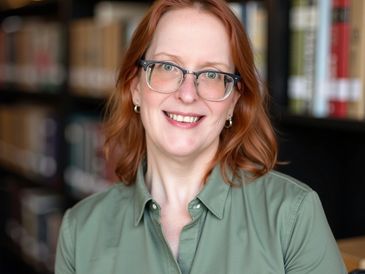 Smiling woman with glasses in a green shirt in a library setting.