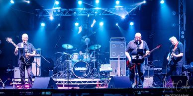 A four-member band performing live on stage with blue lighting.