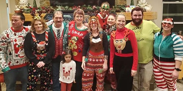 Group in Christmas-themed outfits smiling indoors.