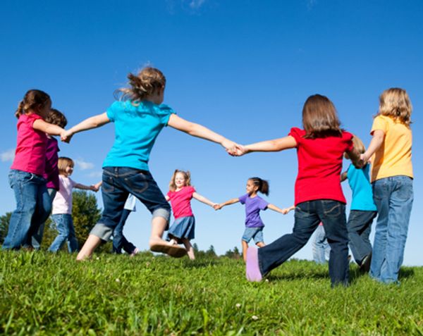 Children holding hands and playing in a circle outdoors.