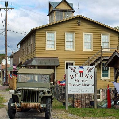 Military jeep stands in front of yellow-brown building with white windows.