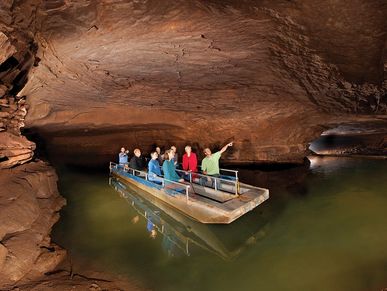 Group on a boat on body of water in a cave. Man in green is pointing upwards.