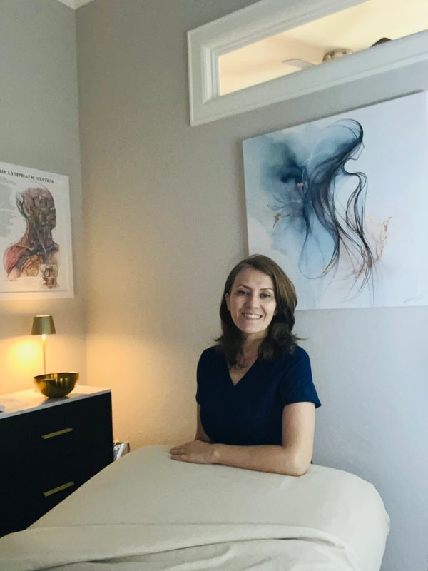 Smiling woman sitting beside a massage table in a softly lit room.