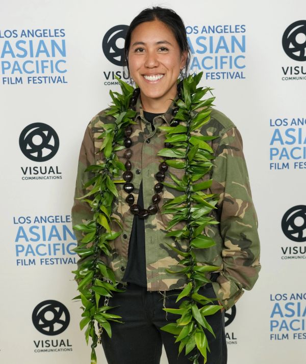 Person in camouflage jacket wearing a green leaf lei and smiling.