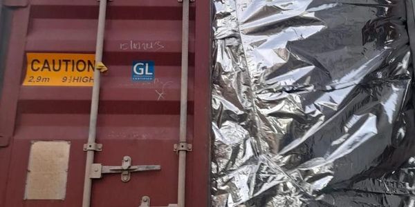 A shipping container door with caution signs and a silver foil covering beside it.