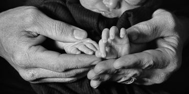 Black and white photo of adult hands gently holding a newborn's tiny hands.