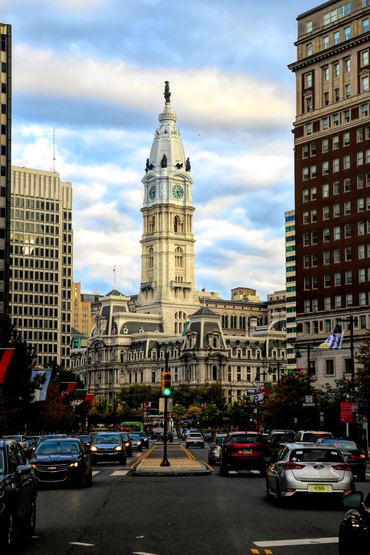 Historic city hall tower surrounded by modern buildings and busy street traffic.