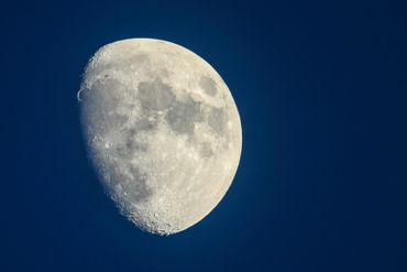 Close-up of a bright waxing gibbous moon against a dark blue sky.