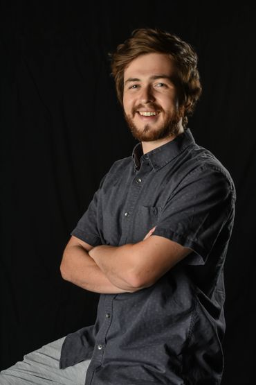 Smiling young man with folded arms against a black background.