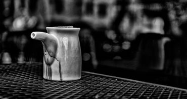 A ceramic teapot on a metal table in black and white.