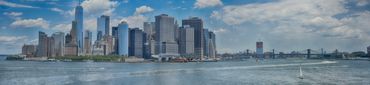 Panoramic view of New York City's skyline with waterfront and cloudy sky.