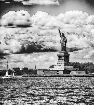 Black and white photo of the Statue of Liberty with dramatic clouds.