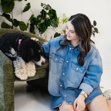 A woman in a denim shirt petting a black and white dog on a green chair.