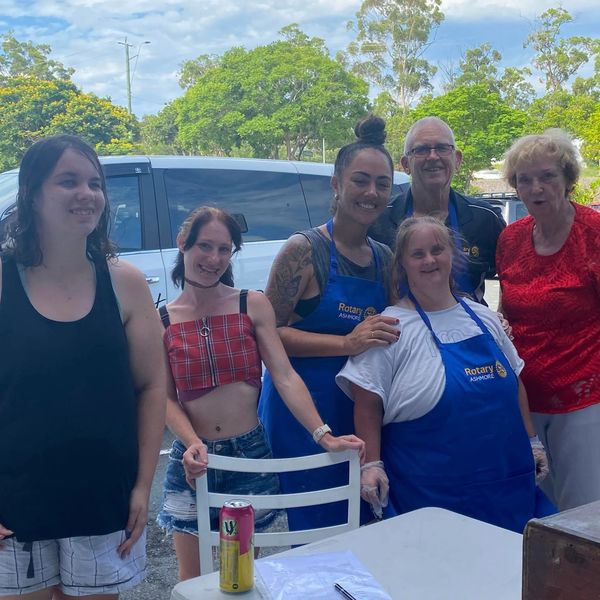 Group of six people smiling outdoors, some wearing Rotary aprons.