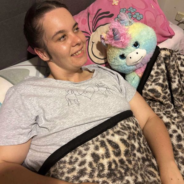 Smiling woman lying in bed with a colorful stuffed unicorn and leopard print blanket.